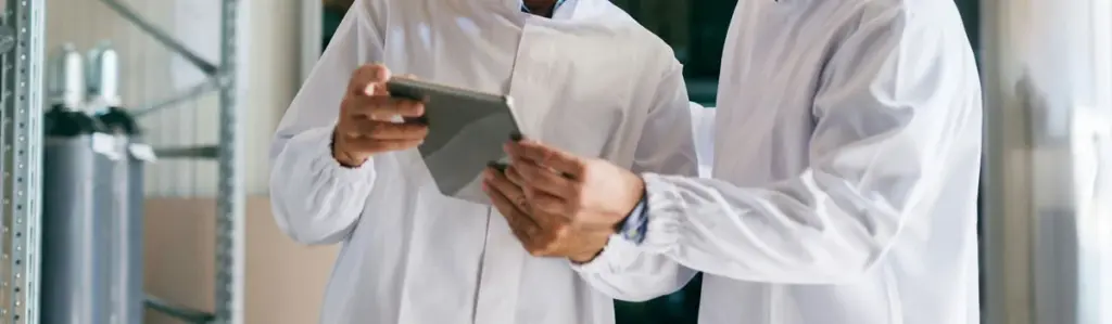 Zwei Personen in Laborkleidung betrachten ein Tablet – symbolisch für die Bewertung einer GxP-konformen SaaS-Plattform für klinische Studien.