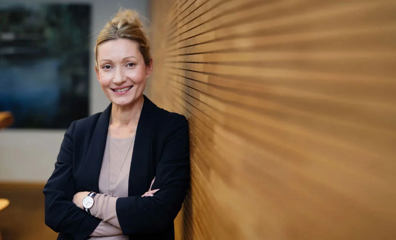 Mitarbeiterin Tanja Topal lehnt an Wand und lächelt – Symbol für Karriere, Teamarbeit und Arbeitsumfeld bei DHC